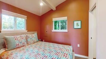 A bedroom with a large bed, two windows, and a door.