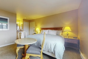 A hotel room with a bed, bedside table, lamp, chair, and a small round table.