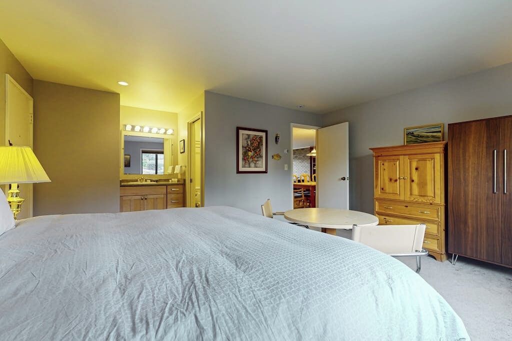 Una habitación de hotel con una cama grande, una mesa de comedor, un espejo y armarios de madera.