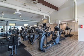 A gym with various cardio machines, weightlifting equipment, and a mirrored wall.
