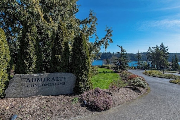 A sign for Admiralty Condominiums with a view of a lake and trees.