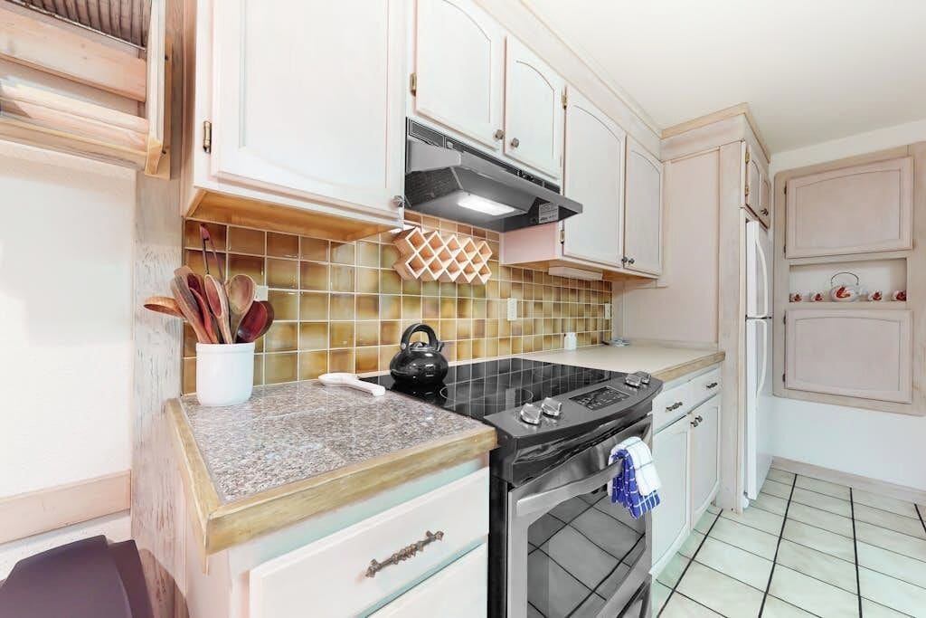Une cuisine avec des meubles blancs, une cuisinière noire et un dosseret carrelé.