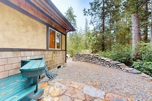 A wooden cabin with a stone patio and a bench.