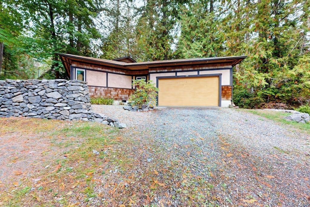 A modern house with a garage, surrounded by a stone wall and gravel driveway.