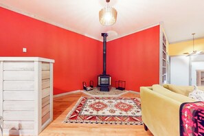 A room with a red wall, a white cabinet, a yellow sofa, a patterned rug, a black fireplace, and a chandelier.