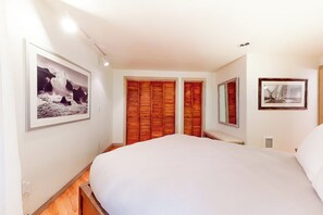 Un dormitori amb un llit gran, un armari de fusta i dos quadres al mur.
