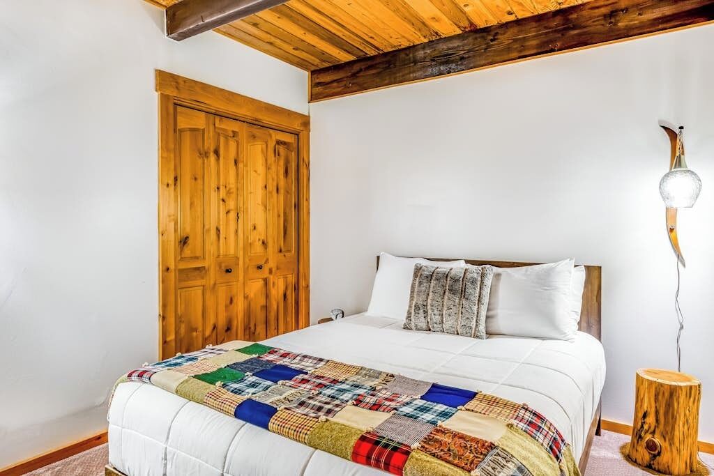 A bedroom with a wooden door, a bed with a quilt, and a nightstand with a lamp.