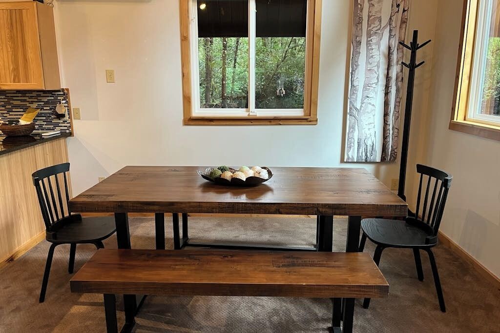 A wooden dining table with four chairs, a bench, and a bowl of fruit on the table.