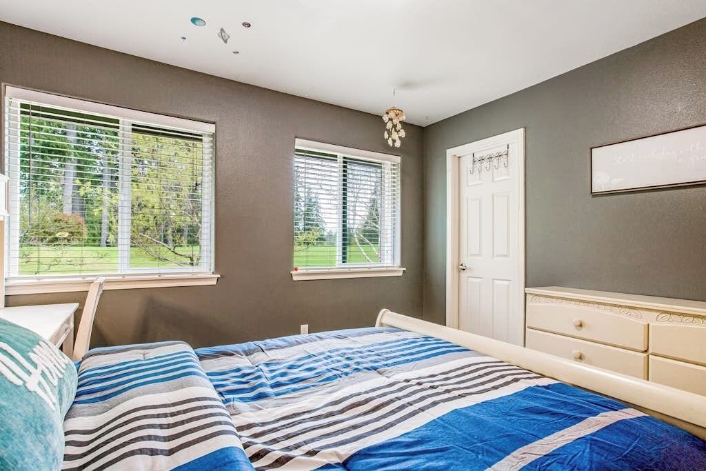 A bedroom with a bed, two windows, a door, and a dresser.
