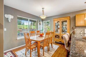 Un comedor con mesa y sillas de madera, una araña y un aparador con puertas de vidrio.