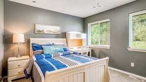 Quarto com cama, mesa de cabeceira, abajur e janela com persianas.
