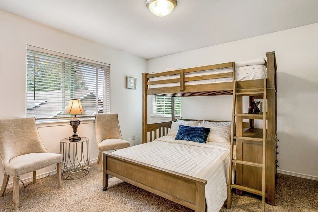 Ein Schlafzimmer mit einem Etagenbett, zwei Stühlen, einem kleinen Tisch mit Lampe und einem Fenster mit Jalousien.