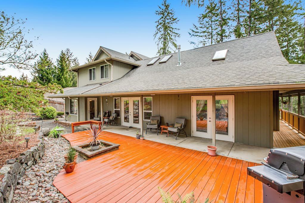 Een huis met een overdekte patio, buitenmeubels en een barbecue.