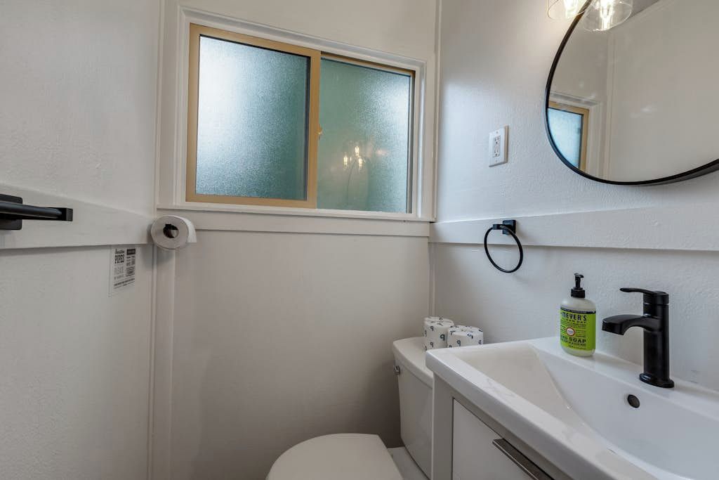 Un baño con inodoro, lavabo, espejo y ventana con vidrio esmerilado.