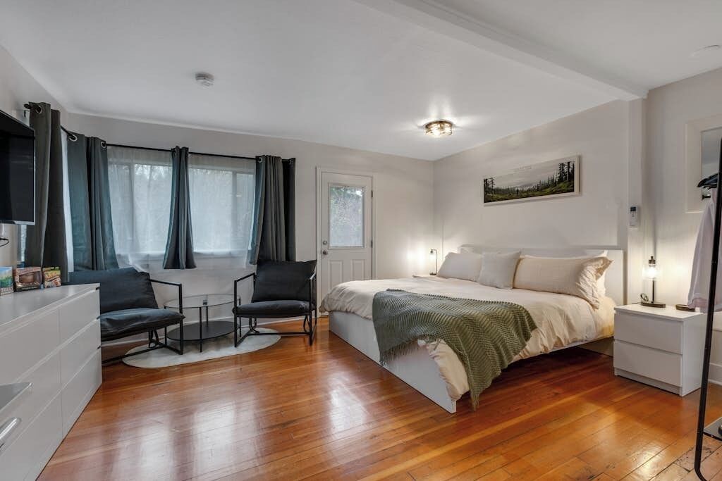 Une chambre à coucher avec un lit, des tables de chevet, une chaise, un bureau et une fenêtre avec des rideaux.