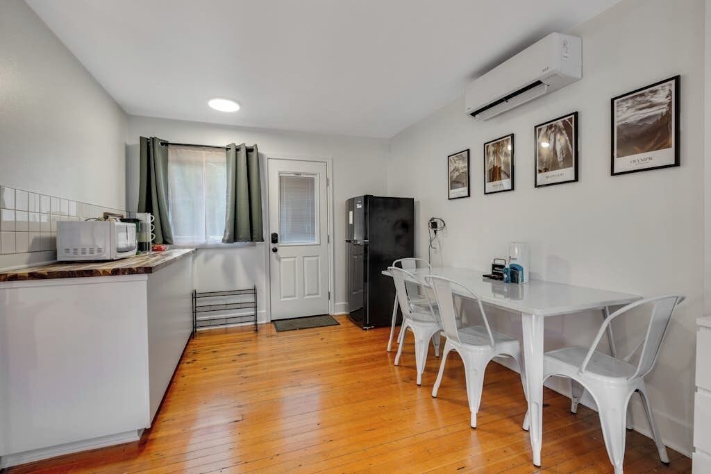 Una cocina compacta con comedor, muebles blancos, un refrigerador y un microondas.