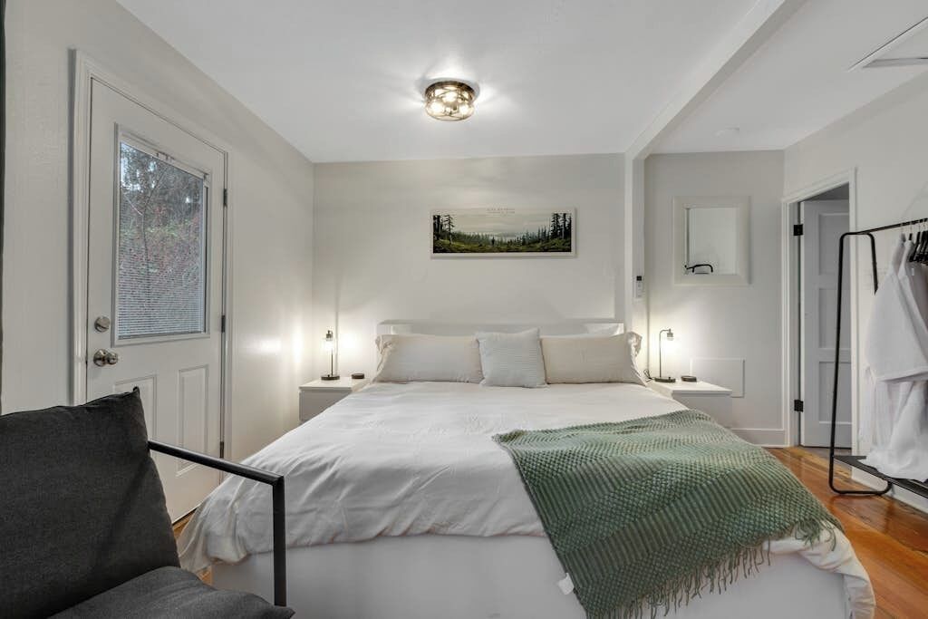 Une chambre à coucher avec un lit, des tables de chevet, une chaise, un tableau au mur et une porte.