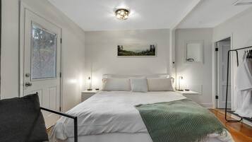 Une chambre à coucher avec un lit, des tables de chevet, une chaise, un tableau au mur et une porte.