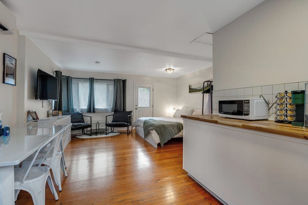 Una habitación pequeña con cama, escritorio, silla, televisor y microondas.