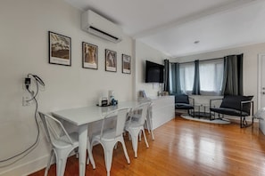 Una sala de estar moderna con una mesa de comedor blanca, sillas de plástico transparente, un televisor de pantalla plana y un sofá.