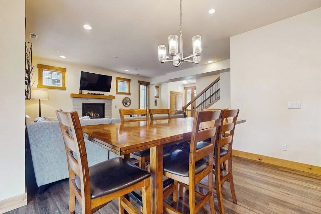 A spacious dining area with a wooden table and chairs, a chandelier, and a fireplace.