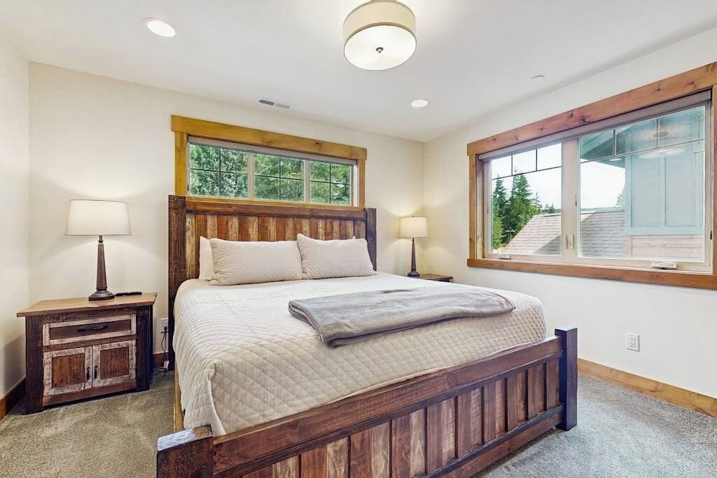 Quarto com cama de madeira, duas mesas de cabeceira, janela com vista e luminária no teto.