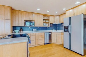 Eine moderne Küche mit Holzschränken, einem Edelstahlkühlschrank, einer Mikrowelle und einem Geschirrspüler.