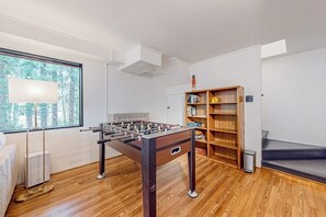 A room with a foosball table, a bookshelf, and a window with a view of trees. - Modern sound view home with expansive deck, mtn view (Port Townsend)