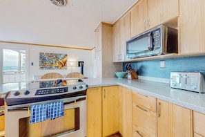 A kitchen with wooden cabinets, a stove, a microwave, and a toaster. - Modern sound view home with expansive deck, mtn view (Port Townsend)