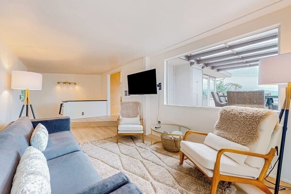 Ein modernes Wohnzimmer mit einer Couch, Sesseln, einem Flachbildfernseher und einem großen Fenster mit Blick.