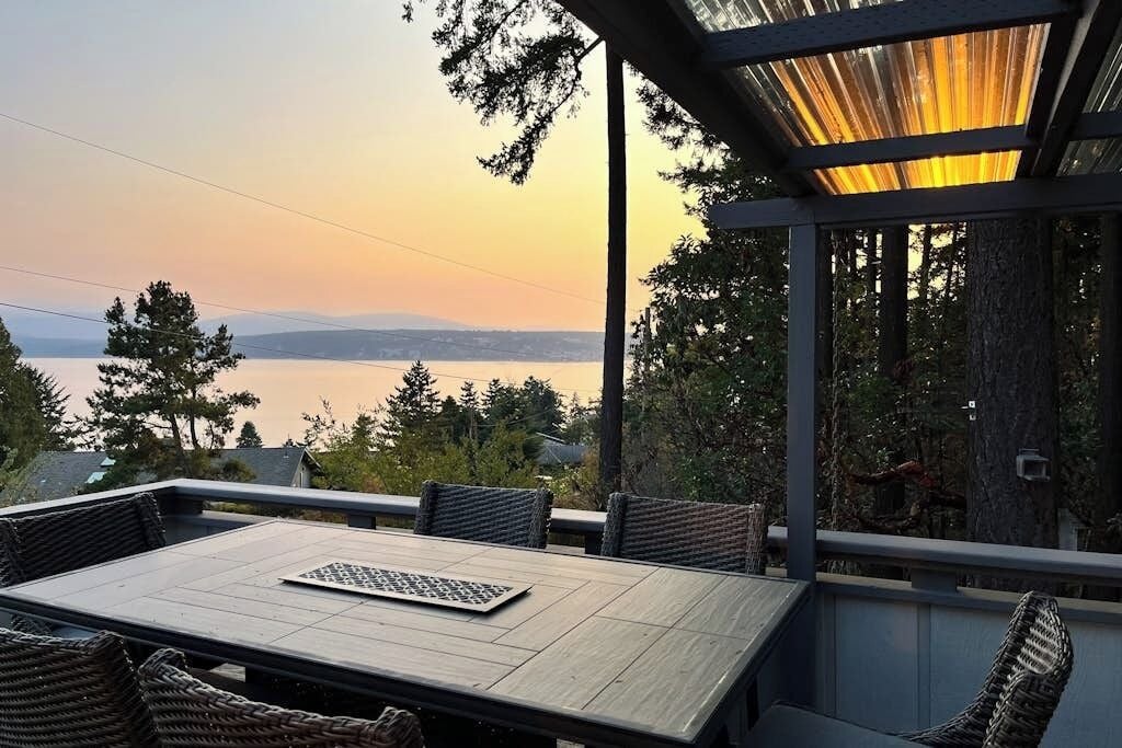 An outdoor patio with a table and chairs, overlooking a body of water and hills.