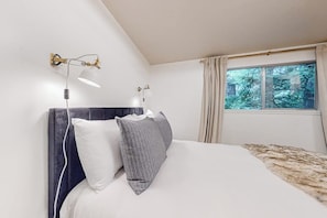 A bedroom with a bed, two wall-mounted lamps, a window with curtains, and a view of trees. - Modern sound view home with expansive deck, mtn view (Port Townsend)