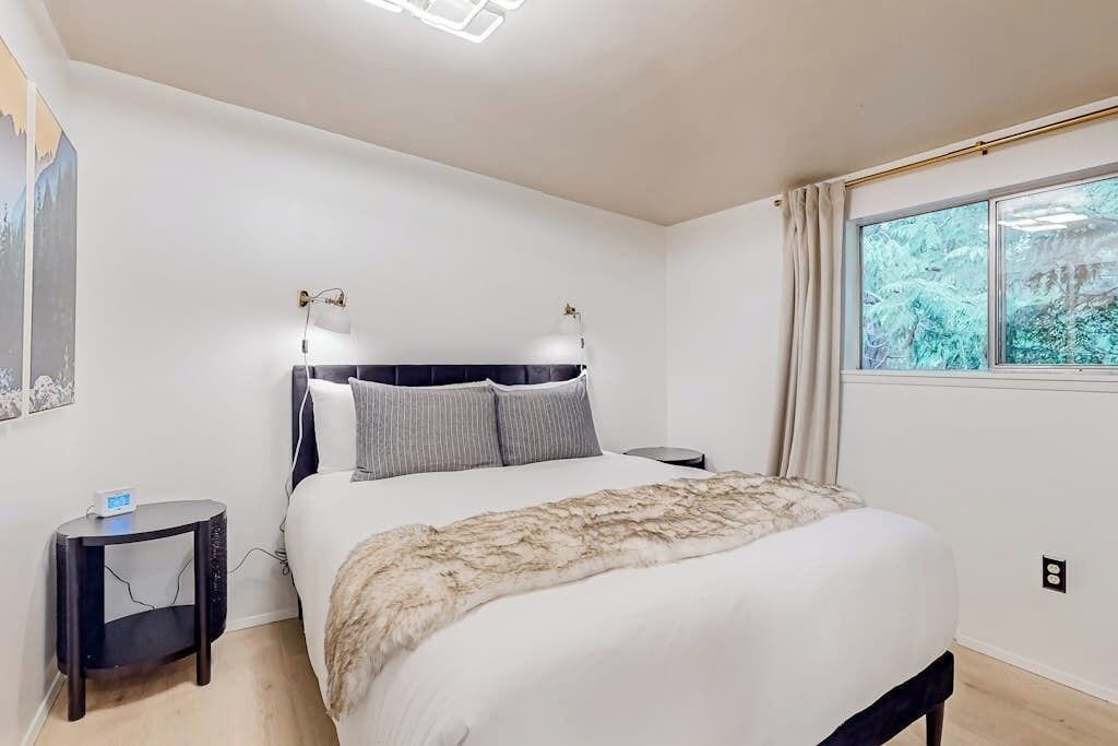 A bedroom with a bed, bedside tables, a window with curtains, and a wall-mounted light fixture.