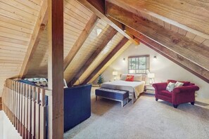 Een slaapkamer met een schuine kap, een bed, een rode bank en een kleine tafel met een lamp.