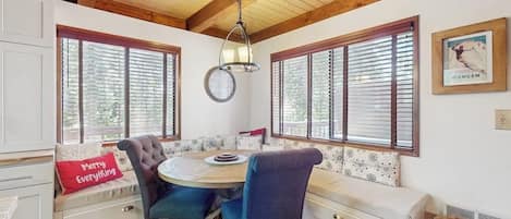 Un coin repas avec une table ronde, des chaises et un banc agrémenté d’un coussin orné de la mention « Joyeuses fêtes ».