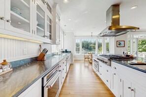 A modern kitchen with white cabinetry, a marble countertop, and a large window offering a view of the outdoors. - Waterfront Home Nearby Island Paradise (Gig Harbor)