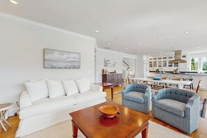 A modern living room with a white sofa, two armchairs, a wooden coffee table, and a dining area with a kitchen in the background. - Waterfront Home Nearby Island Paradise (Gig Harbor)