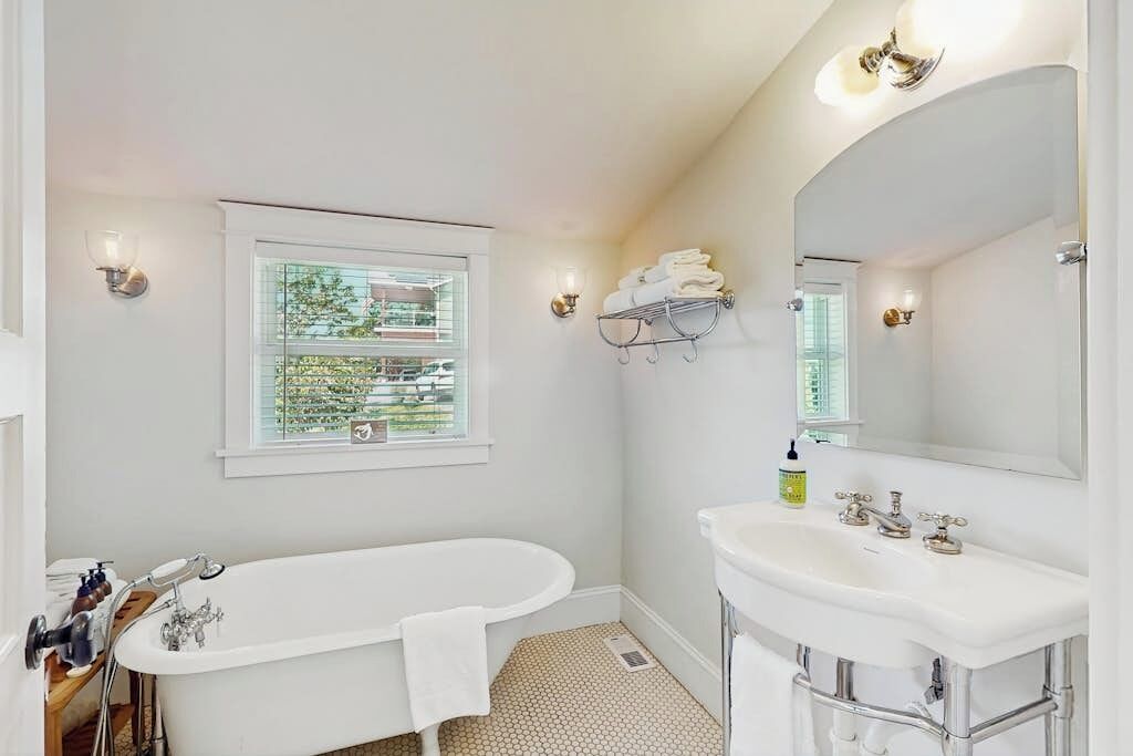 A bathroom with a bathtub, a sink, a mirror, and a window with a view of greenery.