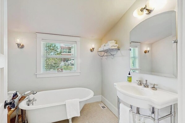 A bathroom with a bathtub, a sink, a mirror, and a window with a view of greenery. - Waterfront Home Nearby Island Paradise (Gig Harbor)