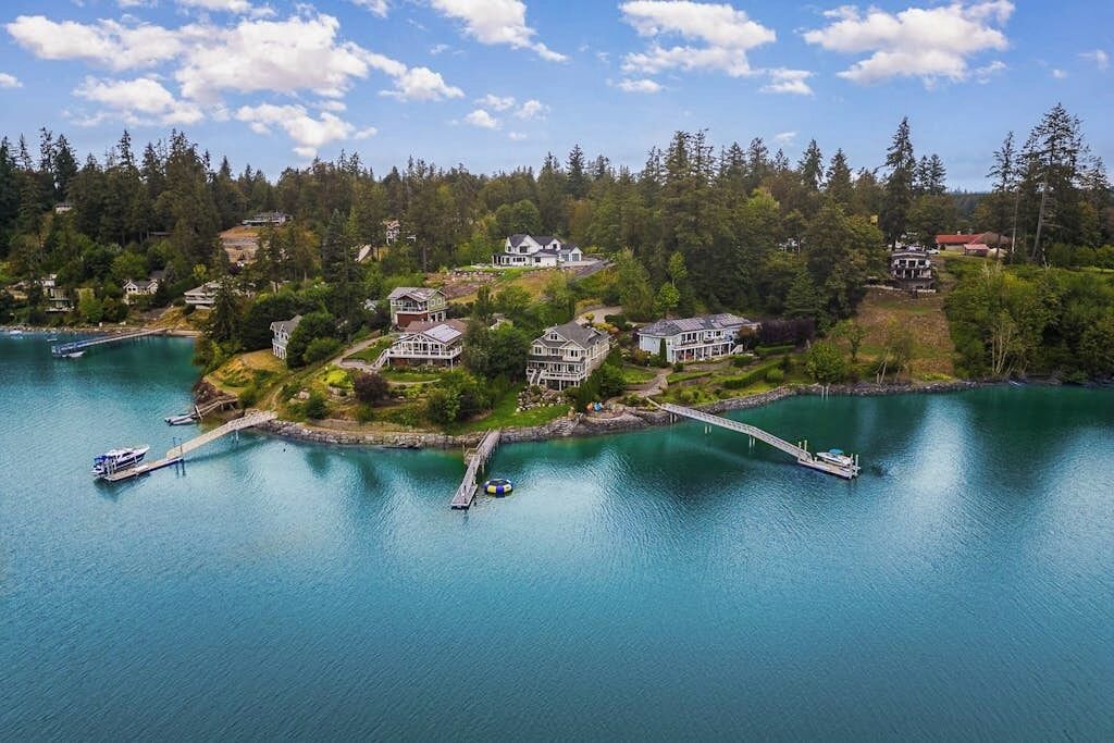 Zona residencial costera con casas, un muelle y un lago tranquilo.