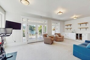 A spacious living room with a treadmill, two sofas, a TV, and a view of a pool. - Waterfront Home Nearby Island Paradise (Gig Harbor)