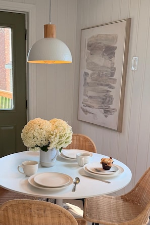 A dining area with a round table set for two, featuring white plates, a white mug, and a white vase with flowers. - Maple & Moss | Cozy 2-Bedroom Retreat in Moncton (Moncton)
