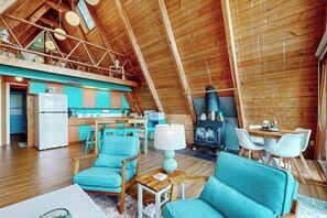 A cozy interior with a high wooden ceiling, a kitchen area with a stove, and seating arrangements.