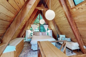 A cozy, wooden interior with a bed, seating area, and a view through a window.