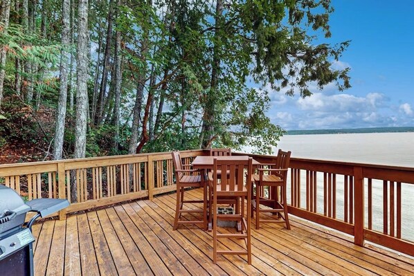 A wooden deck with a grill, seating, and a view of a lake.