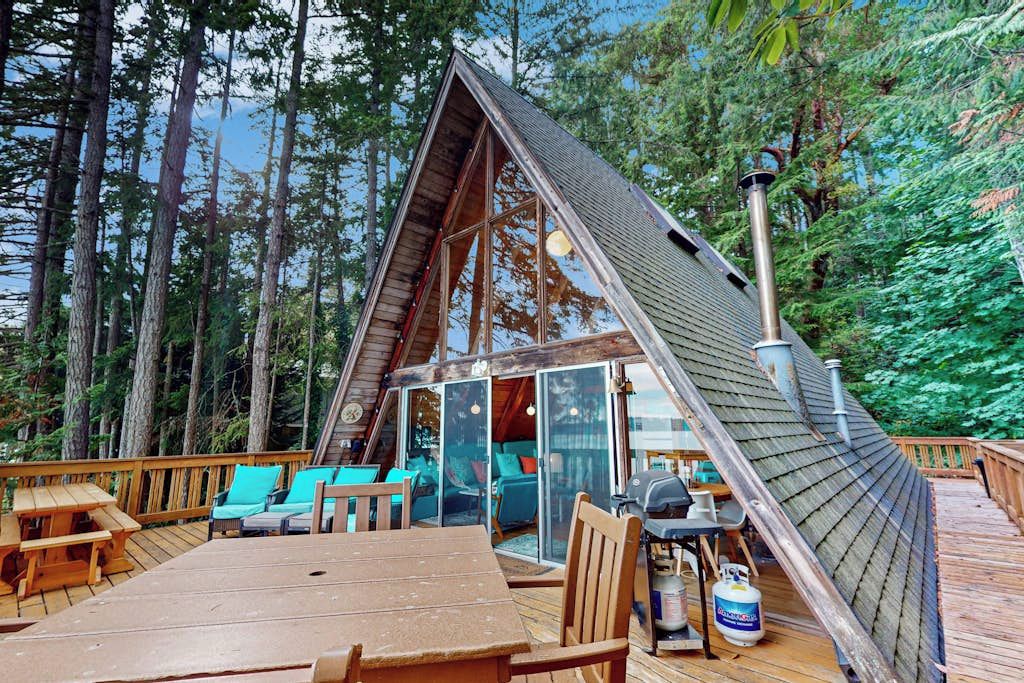 A cabin with a sloped roof, a deck with seating, and a grill area.