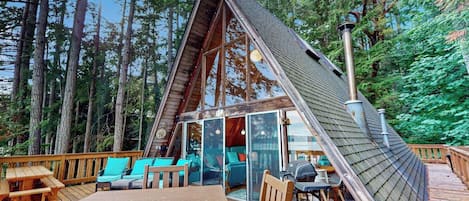 A cabin with a sloped roof, a deck with seating, and a grill area.