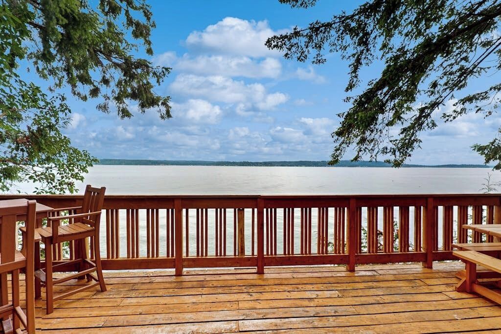 A wooden deck with a railing overlooking a calm body of water, with trees framing the view.