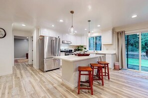 A modern kitchen with a central island, stainless steel appliances, pendant lighting, and a view to the outdoors.