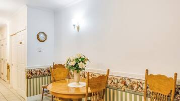 A dining area with a round wooden table, four chairs, a vase with flowers, and a wall clock.